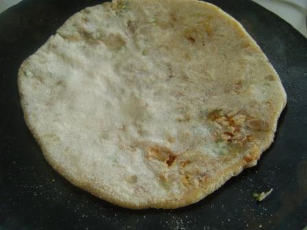 After 30 seconds, you will see that the flat-bread's lower surface has hardened a bit. Now, it is time to flip it. After the flip, spread 1/2 tsp of Oil/Ghee on the flipped surface of the paratha.